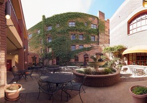 Une terrasse extérieure avec des tables et des chaises, un mur de briques orné de plantes grimpantes et une fontaine.