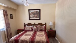 A neatly arranged bedroom with a large bed, a bedside table with a lamp, a framed picture on the wall, and a window with curtains. - Charming Suite on Main Street (Placerville)