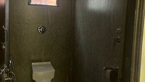 A small, narrow bathroom with a toilet, a window, and a shower area.
