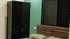 A bedroom with a bed, green bedding, a wardrobe, a window with a black frame, and an air conditioning unit.