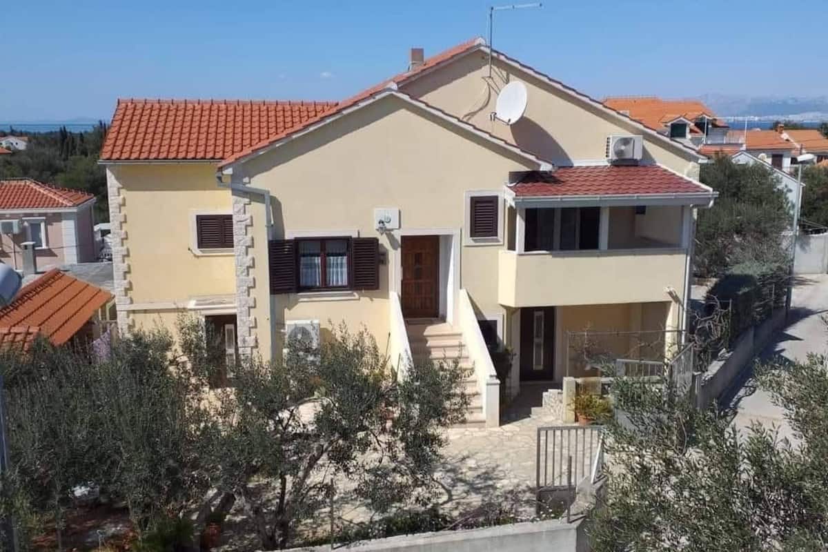 A two-story house with a red-tiled roof, a satellite dish, and a small garden area.