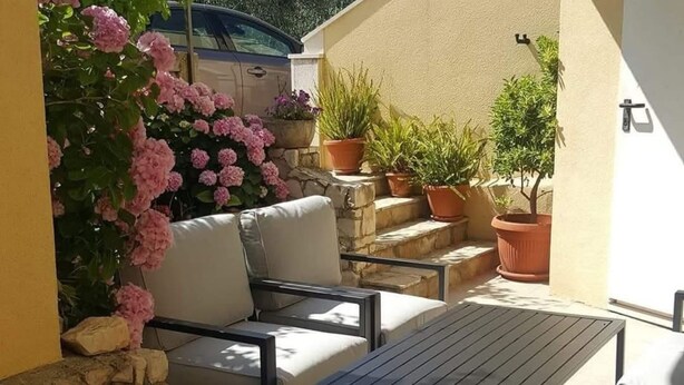 A patio with a sofa and table, surrounded by potted plants and a stone wall. - Apartments Ivan Supetar (Supetar)