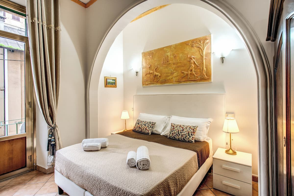 Ein Hotelzimmer mit einem großen Bett, zwei Nachttischlampen, einem Bild an der Wand und einem Fenster mit Vorhängen.