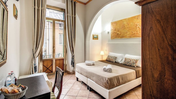 A hotel room with a bed, a desk with a basket of bread, a window with curtains, and a painting on the wall. - GUEST HOUSE GOITO (Rome)