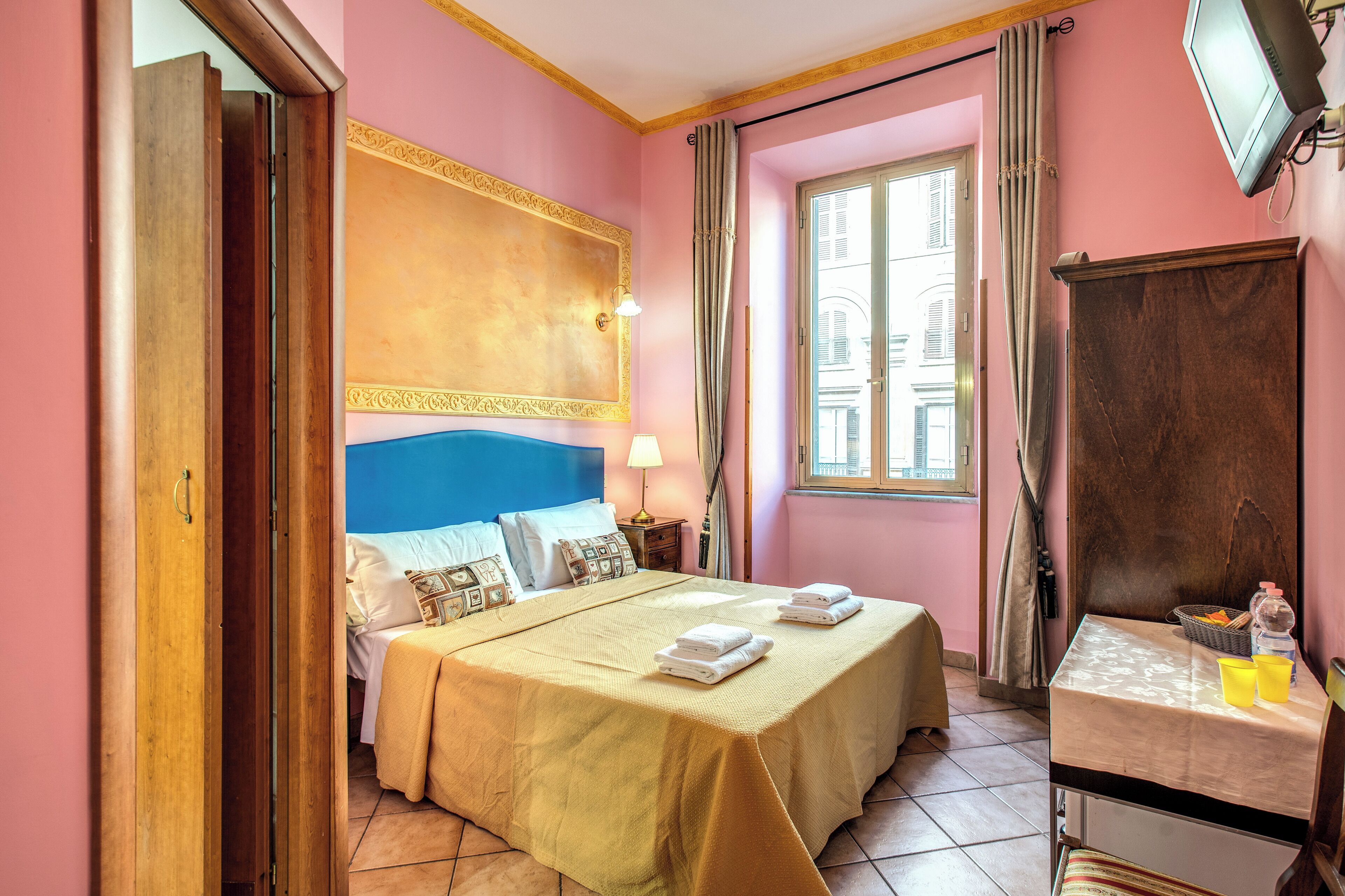 Una habitación de hotel con cama, mesita de noche y ventana con cortinas.
