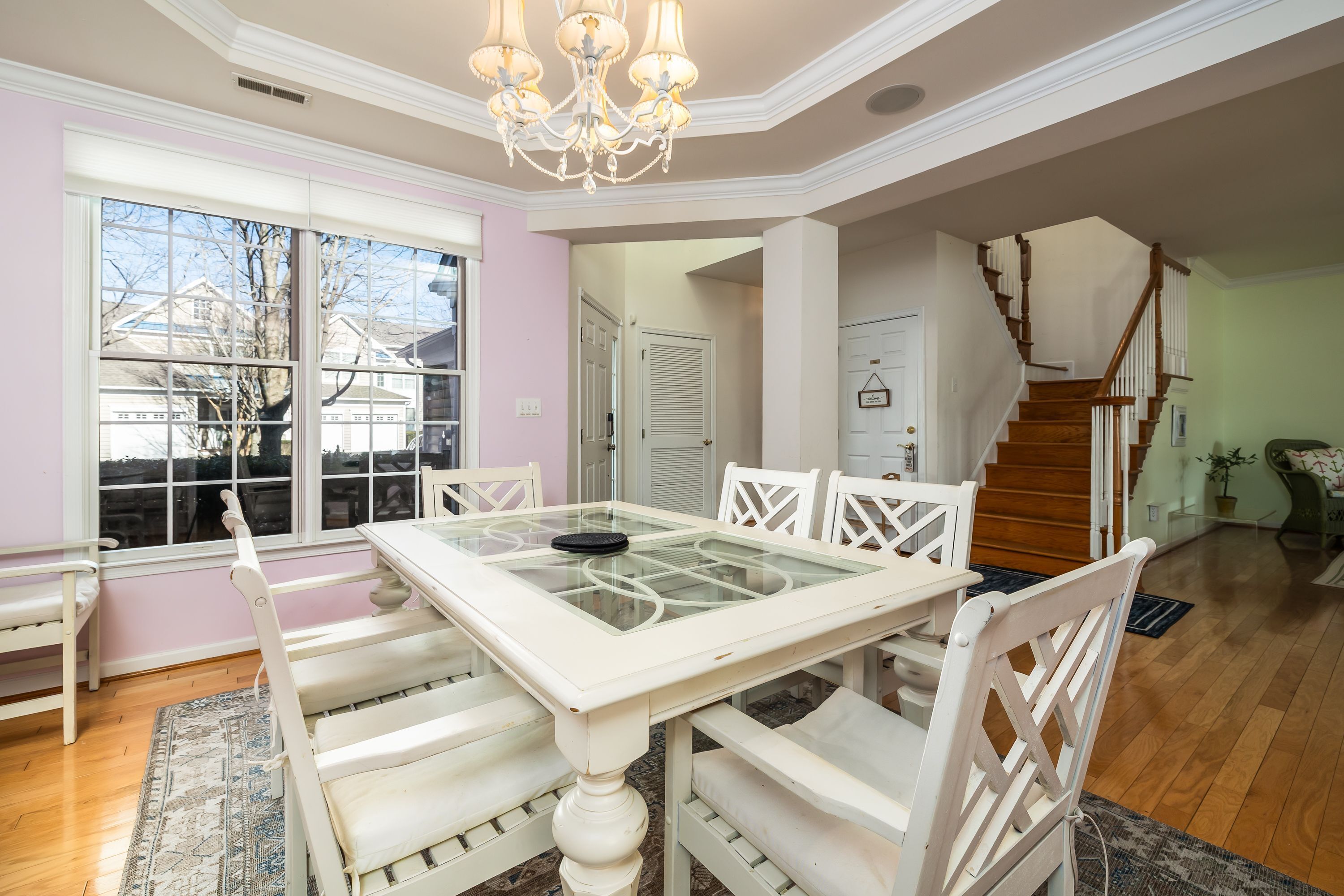 A dining area with a white table and chairs, a chandelier, and a view through large windows.