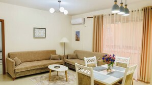 A living room with a sofa, a dining table with chairs, a lamp, and a clock on the wall.