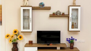 A TV on a wooden stand with a vase of sunflowers and another with blue flowers.
