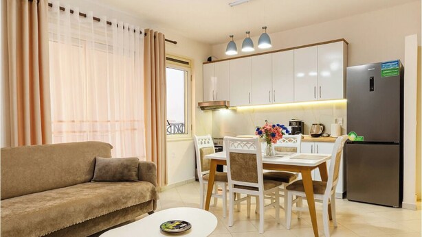 A living room with a sofa, a dining table with chairs, a kitchen area with cabinets and a refrigerator.