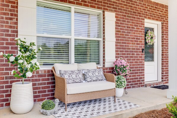A brick house with a white door, a wicker sofa with cushions, and two potted plants. - Water Oaks Retreat Charming 2-bedroom house in Laurel Hill (Laurel Hill)
