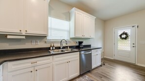 Una cocina con armarios blancos, electrodomésticos de acero inoxidable, encimera negra y suelo de madera.