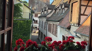 Blick aus einem Fenster auf eine enge Straße mit traditioneller europäischer Architektur, darunter Fachwerkhäuser und ein Schornstein.