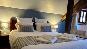 Ein ordentlich bezogenes Bett mit weißer und gestreifter Bettwäsche, zwei Nachttischlampen und einem hölzernen Kopfteil.