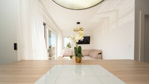 A modern living room with a large wooden table, a mounted TV, and a potted orchid.