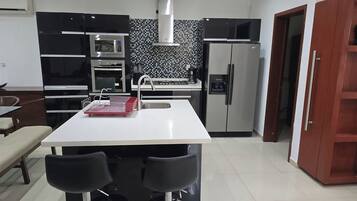 A modern kitchen with a white countertop, stainless steel appliances, a coffee machine, and a red dish rack.