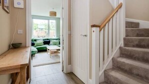 Un pasillo que lleva a una habitación verde con una mesa de madera y una escalera con barandilla de madera.