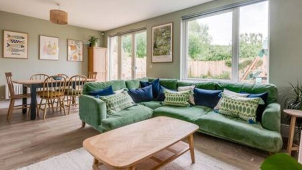 Una sala de estar con un sofá verde, una mesa de centro de madera y un comedor con mesa y sillas.