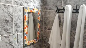 A bathroom with a marble-tiled wall, a sink with a brown basin, a mirror with a colorful frame, and white towels hanging on a rack. - Guest House Peace Love (Porto Seguro)