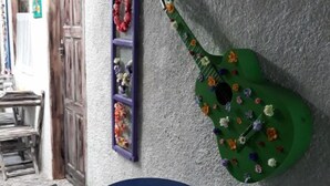 Um quarto com uma guitarra verde fixada na parede, uma prateleira roxa com flores e uma mesa redonda azul.