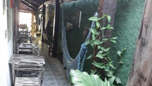 A narrow outdoor corridor with a hammock, large green plants, and wooden furniture. - Guest House Peace Love (Porto Seguro)