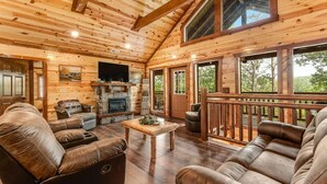 L’intérieur d’une cabane en rondins, avec une cheminée, des canapés en cuir et de grandes fenêtres.