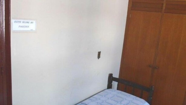 A small room with a single bed, a wooden wardrobe, and a sign on the wall. - Pousada Cristal Limeira (Limeira)