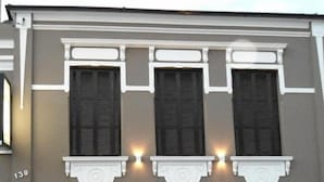 A building facade with three windows, each with shutters, and a black door. - Pousada Cristal Limeira (Limeira)