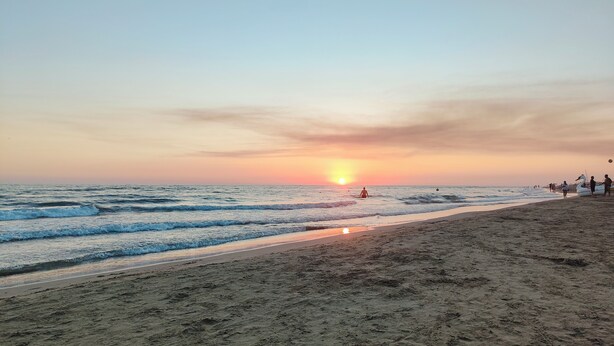 Una playa con un atardecer, olas y un flotador con forma de cisne.