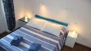 Una cama bien hecha con ropa de cama azul y blanca a rayas, dos almohadas y toallas dobladas. Hay mesitas de noche con lámparas a ambos lados de la cama.