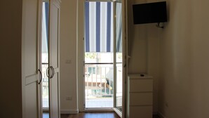Una puerta abierta que da a un balcón con vista a rayas, un pequeño armario blanco y un televisor de pared.