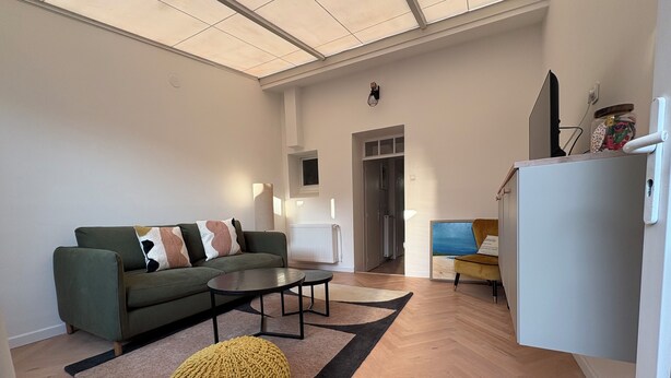 A modern living room with a sofa, coffee table, and ottoman. There is a kitchen area with a refrigerator and a chair. - Pretty 50 m2 fisherman's cottage with exterior (Etaples)