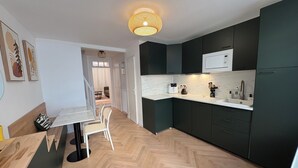 A modern kitchen with dark cabinets, a white countertop, and a herringbone wood floor. There is a dining area with a white table and chairs. - Pretty 50 m2 fisherman's cottage with exterior (Etaples)
