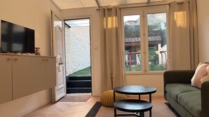 A compact living space with a sofa, a small table, a TV on a cabinet, and a view of a garden through a door. - Pretty 50 m2 fisherman's cottage with exterior (Etaples)