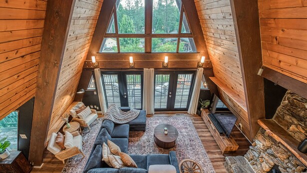 A cozy loft-style room with a large window, a fireplace, and a sectional sofa. - The A-Frame on Toku: Gameroom/HotTub/Firepit/BassLake (North Fork)