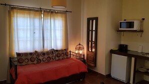 A compact room with a bed, a small kitchenette, a microwave, and a window with curtains. - Posada del Santo Green & Rest (Cerrillos)