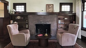 Ein Zimmer mit Kamin, zwei Sesseln, einem Couchtisch und Bücherregalen.