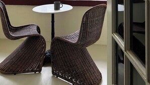 Ein Zimmer mit einem großen Fenster, Korbstühlen, einem kleinen runden Tisch und einem Deckenventilator.
