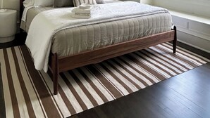 Ein Schlafzimmer mit einem Bett, Nachttischlampen, einem Fenster und einem Streifenmuster-Teppich.