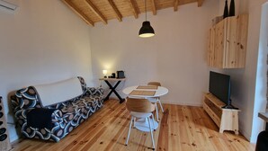 Un salon chaleureux avec un canapé à motifs, une petite table ronde entourée de chaises, un meuble pour la télévision et un luminaire suspendu.