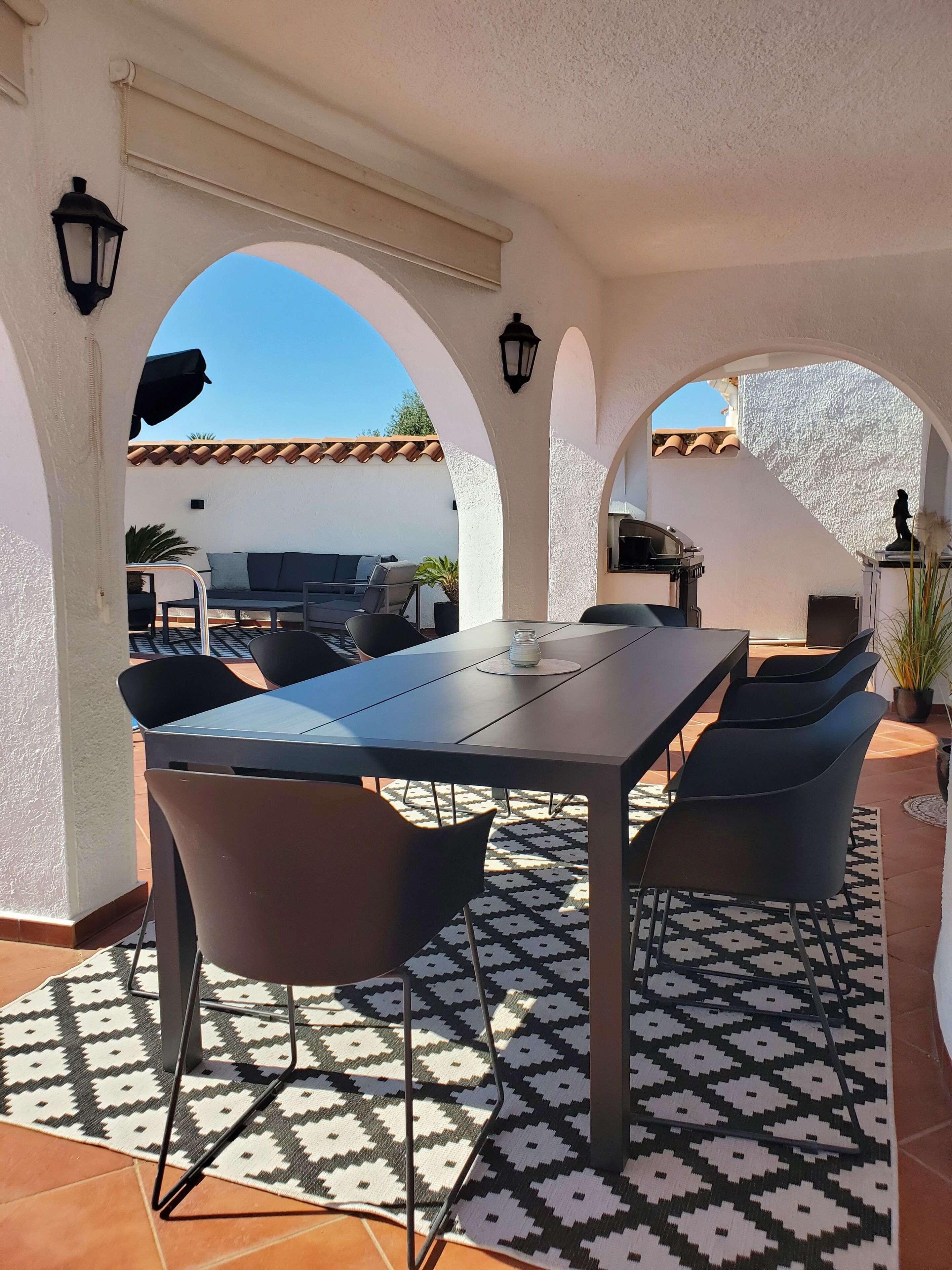 Une terrasse extérieure avec une table et des chaises, entourée d’arcades et agrémentée d’un tapis à motifs.