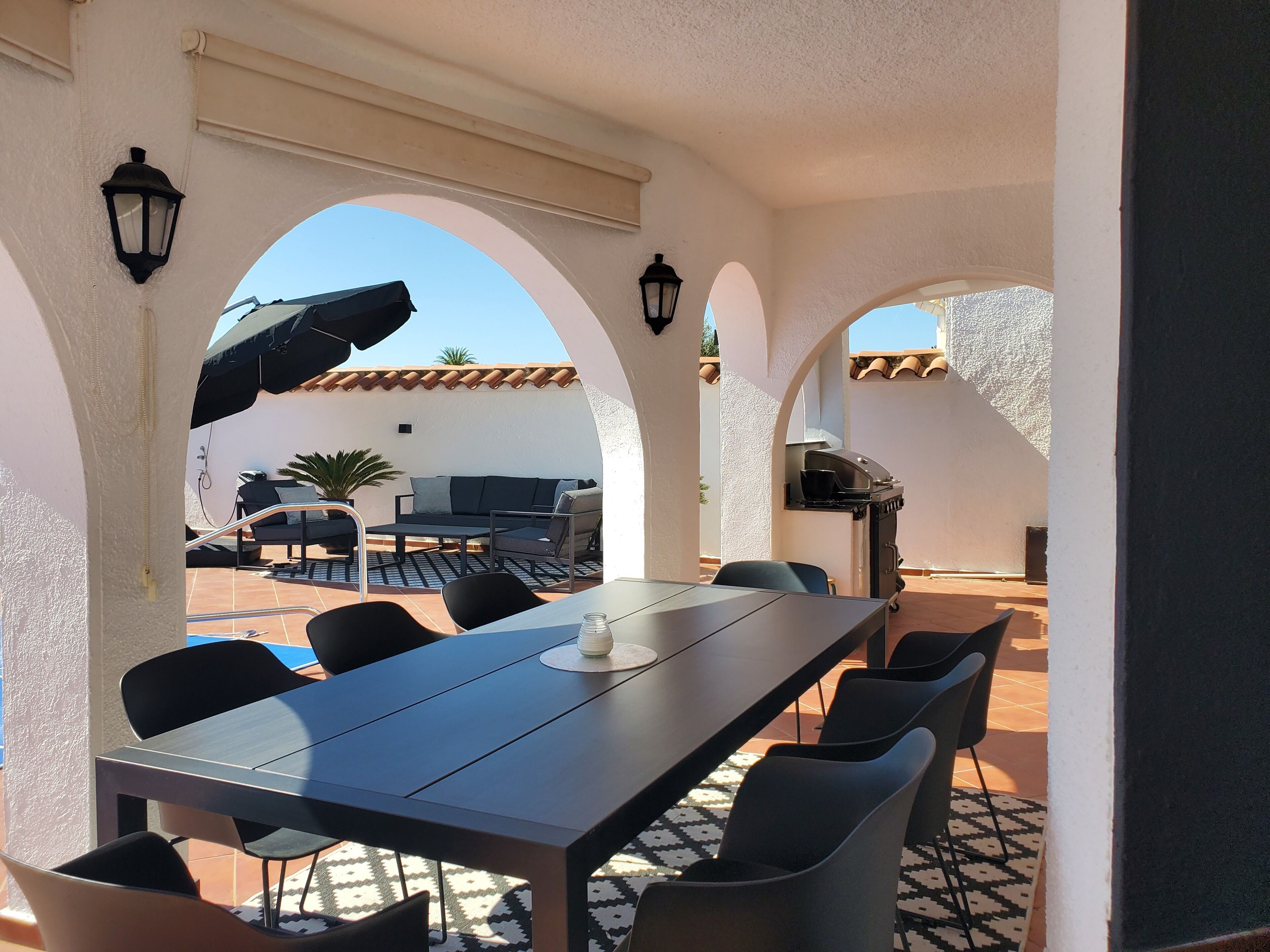An outdoor patio with a long table, chairs, and a grill.
