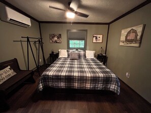 A bedroom with a bed, a ceiling fan, an air conditioning unit, a window, and a wall-mounted picture. - Feisty Ranch Farm Retreat - Private and charming 2-bedroom on 15 acres (Aquone)