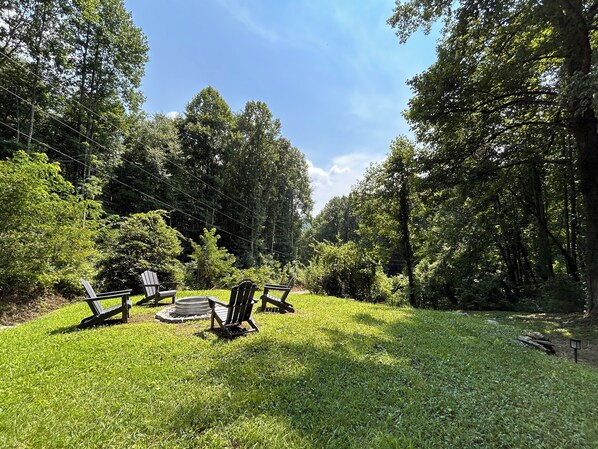 Un espacio al aire libre con césped, una fogata circular y cuatro sillas Adirondack.