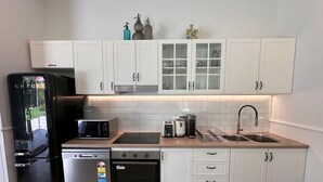 Une cuisine compacte avec des meubles blancs, un réfrigérateur noir, un lave-vaisselle, un four à micro-ondes, un grille-pain et un évier.