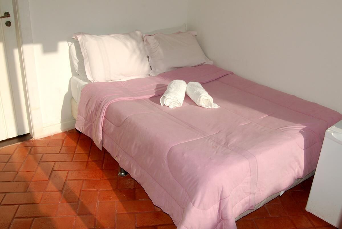 A single bed with pink bedding and two rolled towels on it.