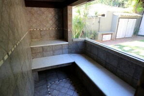 A bathroom with a bench, tiled walls, and a window overlooking a garden. - Pousada Bonfim (Búzios)
