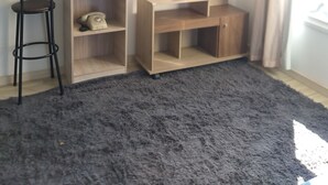 Una habitación con un escritorio de madera, una silla, una estantería con adornos y un televisor de pantalla plana montado en la pared.
