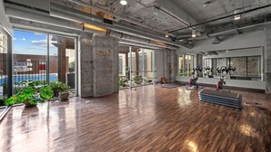 A spacious indoor area with a wooden floor, large windows, and visible gym equipment. - Rodeo Room Downtown Loft | Skyline View, Pool ,Gym & Free Valet Parking (Dallas)