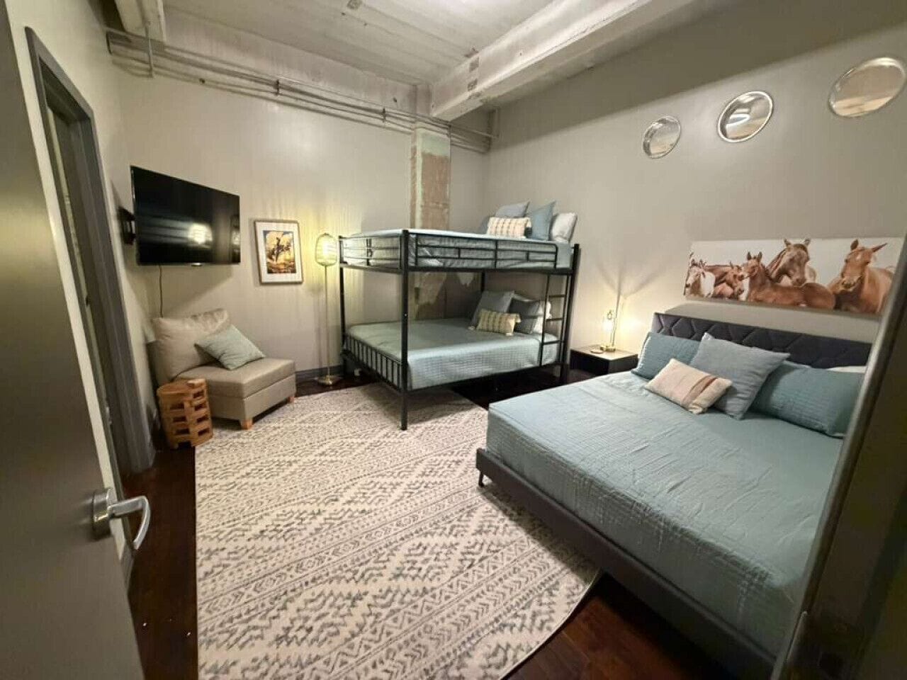 Une chambre avec un lit superposé, un lit simple, un tapis à motifs, une télévision et des œuvres d’art accrochées au mur.