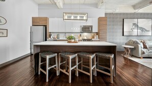 A modern kitchen with a central island, bar stools, a refrigerator, and a microwave. - Rodeo Room Downtown Loft | Skyline View, Pool ,Gym & Free Valet Parking (Dallas)